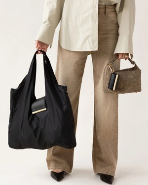 The KEOTE - KEYCHAIN TOTE IN JET BLACK by KEOTE is a reusable black tote made of crinkled fabric, shown flat with a matching small carrying case—ideal as a compact bag for easy storage and daily use.