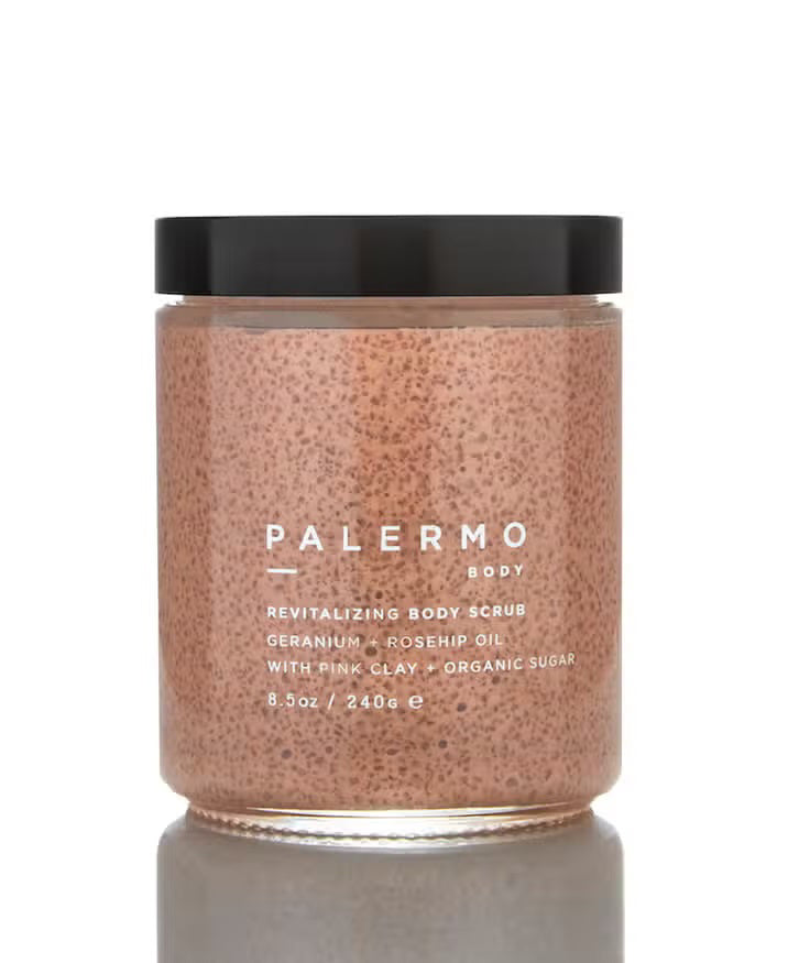 The PALERMO BODY GERANIUM AND ROSE HIP BODY SCRUB comes in a clear jar with a black lid. This pink scrub, rich in French pink clay and organic sugar granules, offers revitalizing benefits. The label lists ingredients such as geranium, rosehip oil, and organic sugar. This 8.5 oz / 240 g jar also features aromatherapeutic properties.
