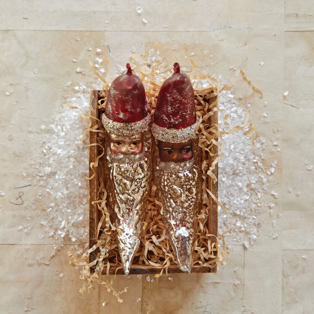 The CREATIVE COOP HAND PAINTED MERCURY GLASS SANTA MOON ORNAMENT features a crescent moon shape with a red tip, silver glitter accents, and a hanging string—perfect for adding festive charm to your Christmas tree.