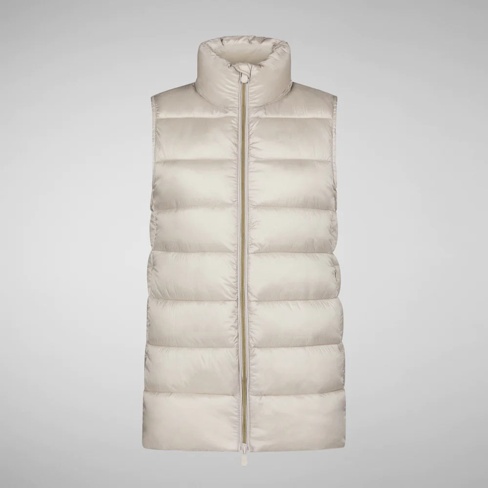 A person wearing a black cap, sunglasses, the SAVE THE DUCK - CORAL PUFFER VEST with animal-free down from SAVE THE DUCK over a black long-sleeve top, beige wide-legged pants, and black ankle boots stands against a plain background. The outfit appears to be styled for colder weather.