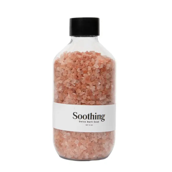 A clear plastic bottle with a black cap is filled with pink Himalayan salt crystals. The white label on the bottle reads &quot;BOTANICAL BATH SOAK - SOOTHING DETOX&quot; by GIFTEN MARKET, featuring essential oils and a net weight of 16 oz.