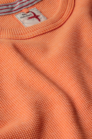 The RELWEN - BI-WAFFLE CREW IN CITRUS, a long-sleeved, citrus orange waffle-knit cotton sweater from RELWEN, is laid flat on a white background. It features ribbed cuffs, hem, and collar with a small visible fabric tag near the hem.