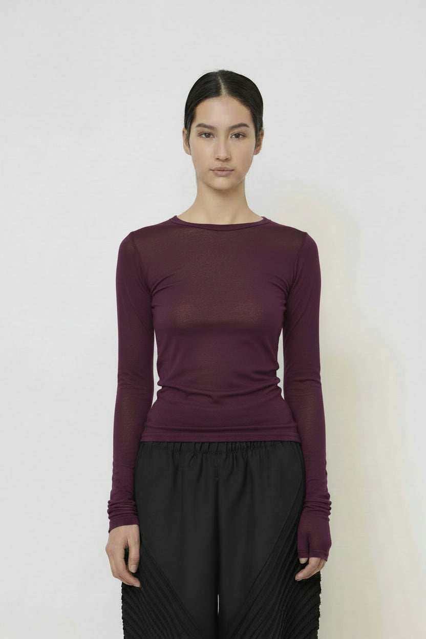 A woman with long dark hair in a low ponytail stands in profile against a plain light background, wearing the MEIMEIJ MESH LAYERING TOP by MEIMEIJ in red and a black skirt for a minimalist Italian fashion look.