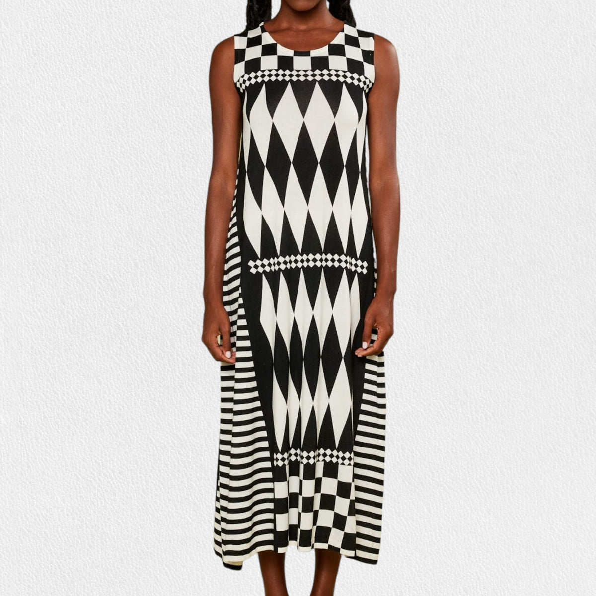 A person is wearing the IN BED WITH YOU - LONG KNIT DRESS featuring a sleeveless, knee-length design and a striking geometric pattern. The dress, from the Italian brand IN BED WITH YOU by CLAUDIOLAI SRL, showcases alternating squares and circles in vibrant prints of red, yellow, purple, and white set against a plain white textured background.