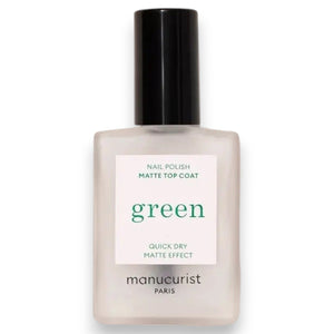 A hand with light blue painted nails holds a bottle of MANUCURIST - GREEN™ Nail Polish Matte Top Coat by MANUCURIST INC, featuring a black cap and clear plant-based formula, against a beige background.