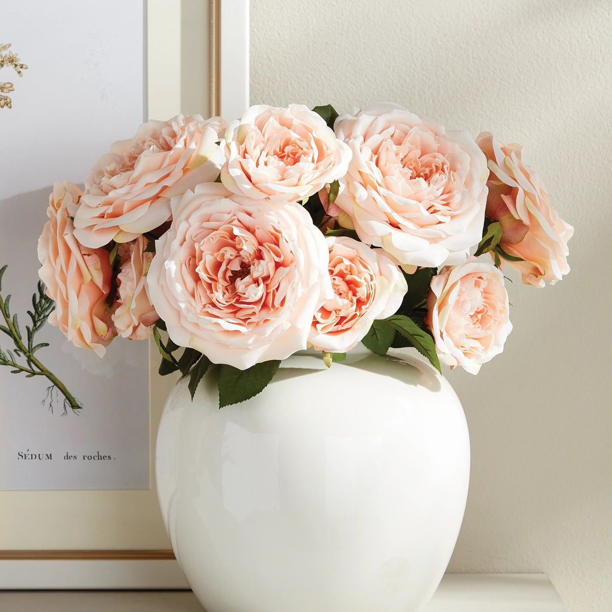 The NAPA HOME AND GARDEN - ENGLISH ROSE STEM features two large, pale peach roses with life-like petals and lush green leaves, tied with a natural raffia ribbon against a plain white background.