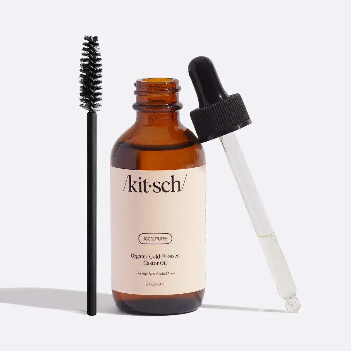 A brown glass bottle labeled "KITSCH - 100% CASTOR OIL" is set between a black mascara wand and a clear oil dropper. Renowned for supporting hair growth and moisturizing cuticles, this beauty essential is displayed on a plain white background.