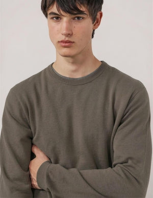 A person wearing the HARTFORD Extra-Fine Merino Wool Crew Pullover in Mushroom and beige pants stands with hands in pockets against a white background.