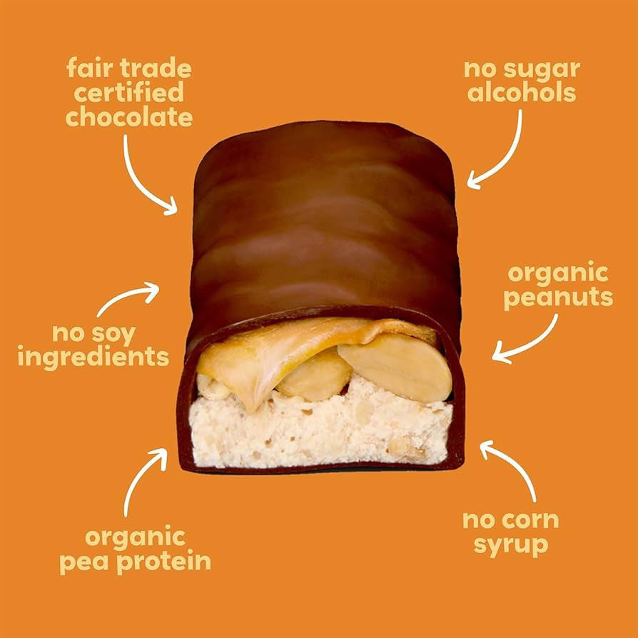 An orange-wrapped UNREAL - DARK CHOC CARAMEL PEANUT NOUGAT BAR with a bite revealing layers of caramel, peanuts, and nougat inside. Crafted with non-GMO ingredients, this healthier candy bar alternative features the product name and flavor in white text on the wrapper under the UNREAL brand.