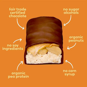 An orange-wrapped UNREAL - DARK CHOC CARAMEL PEANUT NOUGAT BAR with a bite revealing layers of caramel, peanuts, and nougat inside. Crafted with non-GMO ingredients, this healthier candy bar alternative features the product name and flavor in white text on the wrapper under the UNREAL brand.