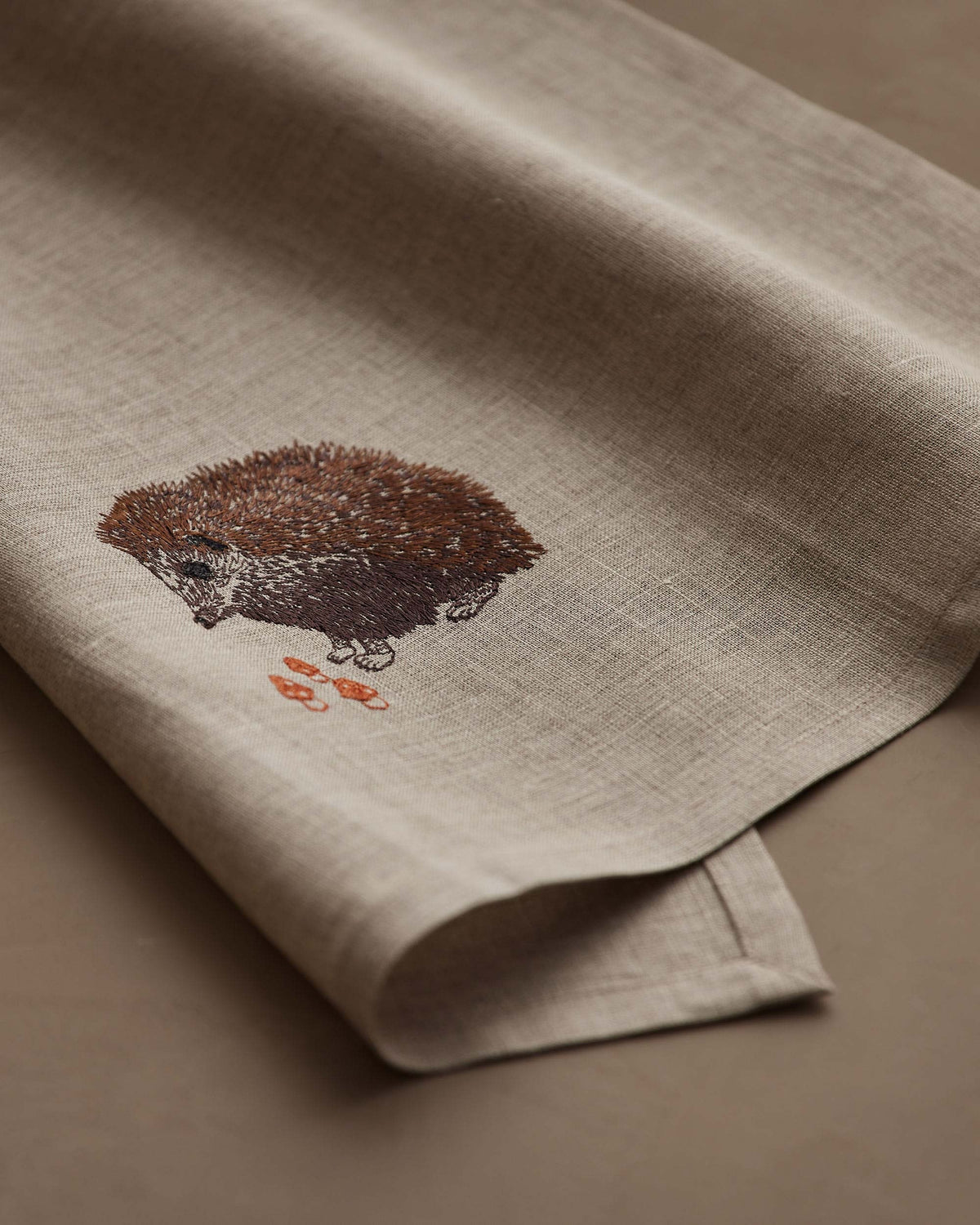 A HEDGEHOG WITH MUSHROOMS LINEN TEA TOWEL by CORAL & TUSK hangs from the handle of a white stove in a kitchen.
