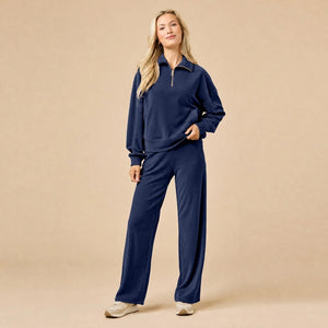 A woman seated on the floor wearing a Softies - Serenity 1/4 Zip Top with Wide Leg Pant lounge set in midnight, featuring a navy blue quarter-zip pullover and matching wide-leg lounge pants.
