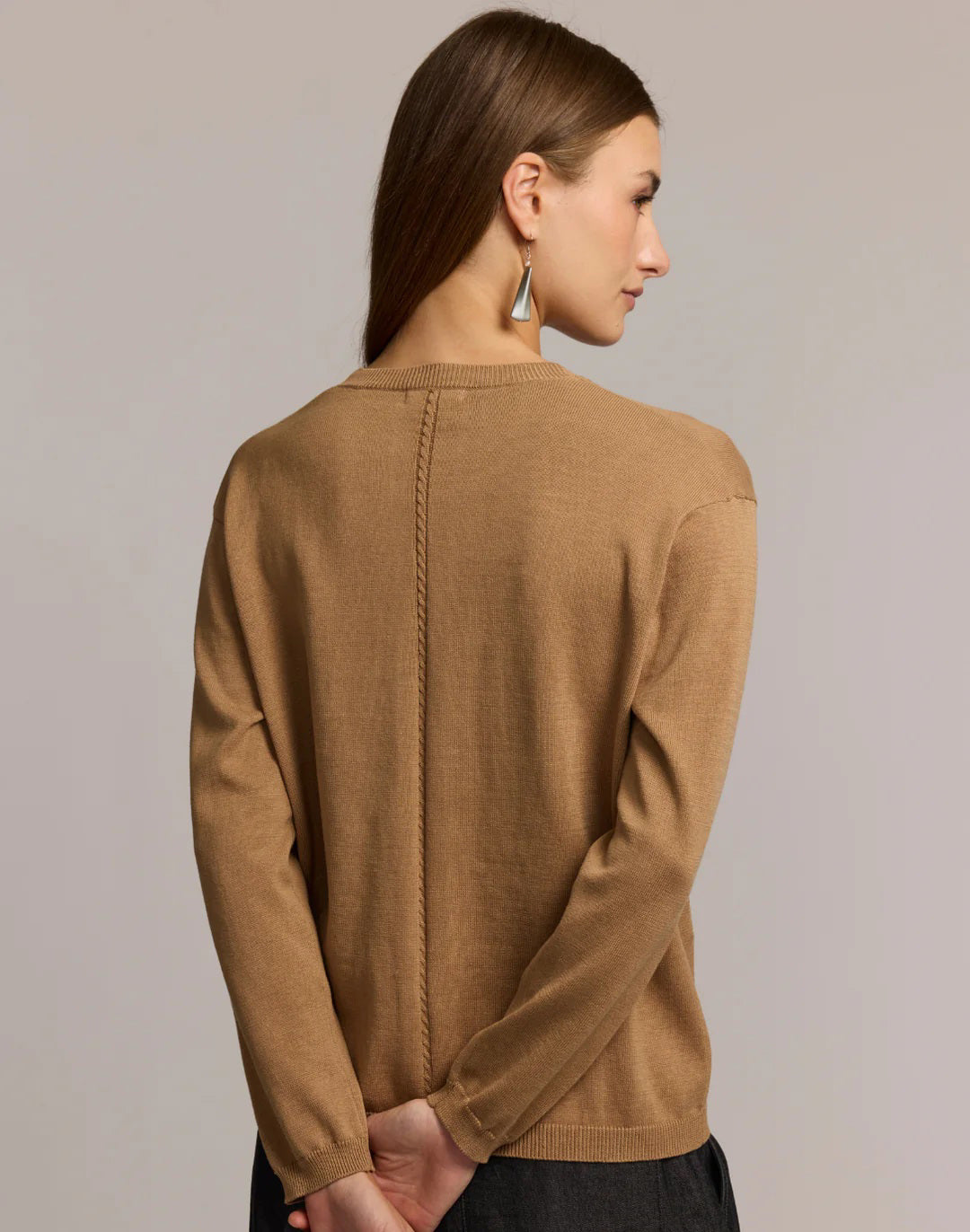 A woman with straight brown hair wears the HINSON WU CASSIE Long Sleeve Cotton Silk Cardigan in camel, styled with black pants. She poses confidently, one hand to her chin, against a neutral backdrop.