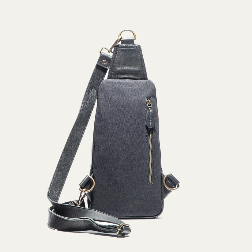 The WILL LEATHER GOODS - ZIP AROUND SLING BAG IN BLACK is a full-grain leather sling bag with gold zippers and buckle, small front pocket, adjustable strap, and top hanging loop, shown against a plain white background.