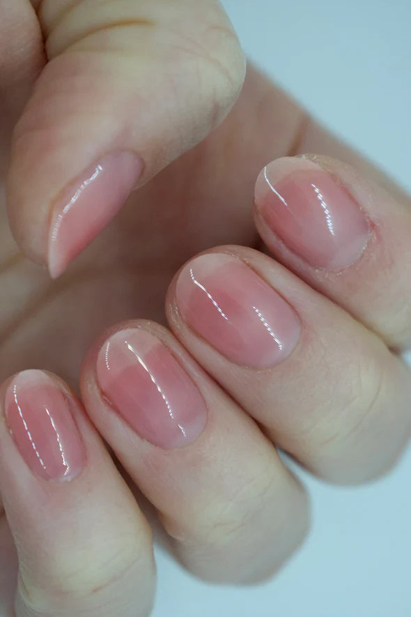 A glass bottle of TENOVERTEN - NAIL POLISH from the brand TEN OVER TEN, featuring a white cap and a dusty pink nail color. The front label displays "TEN OVER TEN" in white uppercase letters. This vegan, eight-free formula ensures both beauty and peace of mind. The background is plain and light-colored.