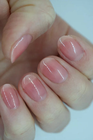 A glass bottle of TENOVERTEN - NAIL POLISH from the brand TEN OVER TEN, featuring a white cap and a dusty pink nail color. The front label displays "TEN OVER TEN" in white uppercase letters. This vegan, eight-free formula ensures both beauty and peace of mind. The background is plain and light-colored.