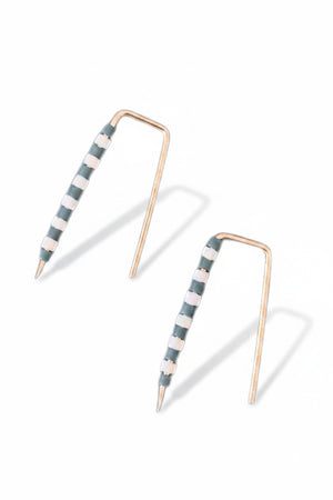 The ALICE RISE - LITTLE QUILL EARRINGS IN SLATE BLUE STRIPE feature unique 14k gold filled posts adorned with alternating white and green beads, arranged parallel on a textured light gray surface.