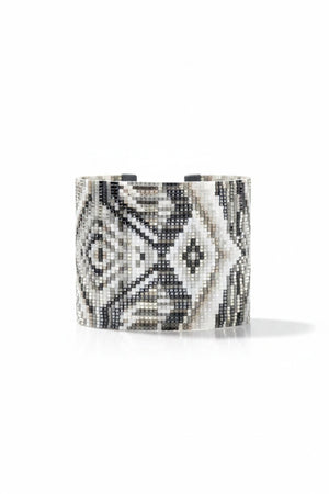 The JULIE ROFMAN - HORIZON CUFF from JULIE ROFMAN JEWELRY is a handwoven glass beaded delica bracelet that showcases an intricate geometric pattern in black, white, and gray. The design includes diamond shapes and symmetrical lines for a mosaic-like appearance, finished with an adjustable buckle clasp to ensure a perfect fit.
