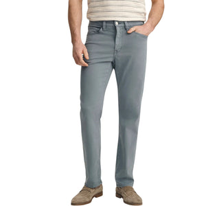 A man stands with his back to the camera against a plain light background, wearing a beige striped short-sleeve shirt, 34 HERITAGE Charisma Relaxed Straight Leg Pant in Flint Stone, brown suede shoes, and sunglasses.