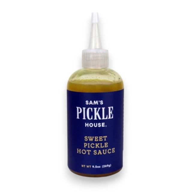 A squeeze bottle labeled “THE PICKLE HOUSE - SWEET PICKLE HOT SAUCE” features a dark blue label with white text. The bottle holds a greenish-yellow, sweet and hot sauce that’s ideal as a salad dressing and comes with a pointed nozzle cap.