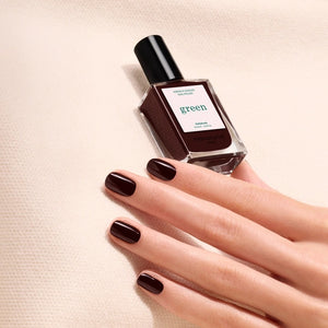 A bottle of MANUCURIST INC GREEN™ Nail Polish in the shade Hollyhock, featuring a dark burgundy color and a black cap.
