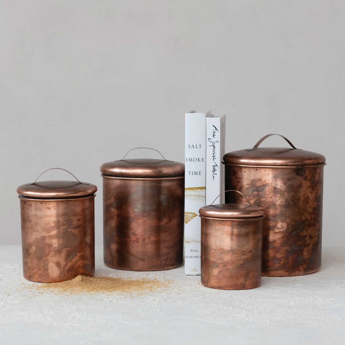 A top view of the CREATIVE COOP STAINLESS STEEL CANISTERS IN OXIDIZED COPPER FINISH, SET OF 4, featuring matching copper lids and arranged symmetrically on a white background.