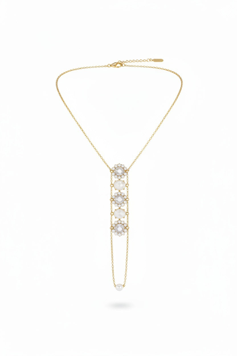 A beige necklace display stand showcases the GOLDISH - FLOWER WHITE MOONSTONE AND WHITE PEARL LADDERS TO BLISS NECKLACE, featuring five gemstones in a vertical, sacred geometry-inspired design. The plain white background enhances its elegance.