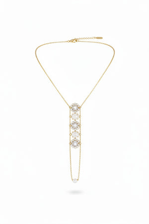 A beige necklace display stand showcases the GOLDISH - FLOWER WHITE MOONSTONE AND WHITE PEARL LADDERS TO BLISS NECKLACE, featuring five gemstones in a vertical, sacred geometry-inspired design. The plain white background enhances its elegance.