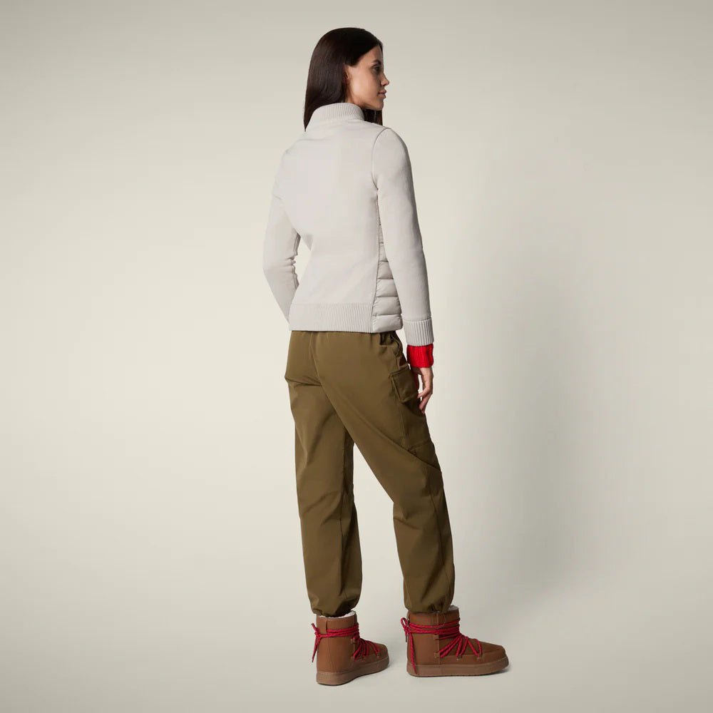 A woman with straight brown hair and a neutral expression models the SAVE THE DUCK - ZILIA JACKET in light gray, styled with olive cargo pants, red socks, and tan boots—showcasing effortless transitional layering.