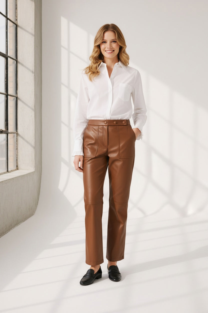 A person wearing high-waisted brown leather pants, a white long-sleeve shirt, and brown heeled ankle boots, standing against a plain light background. The person's face is not visible.