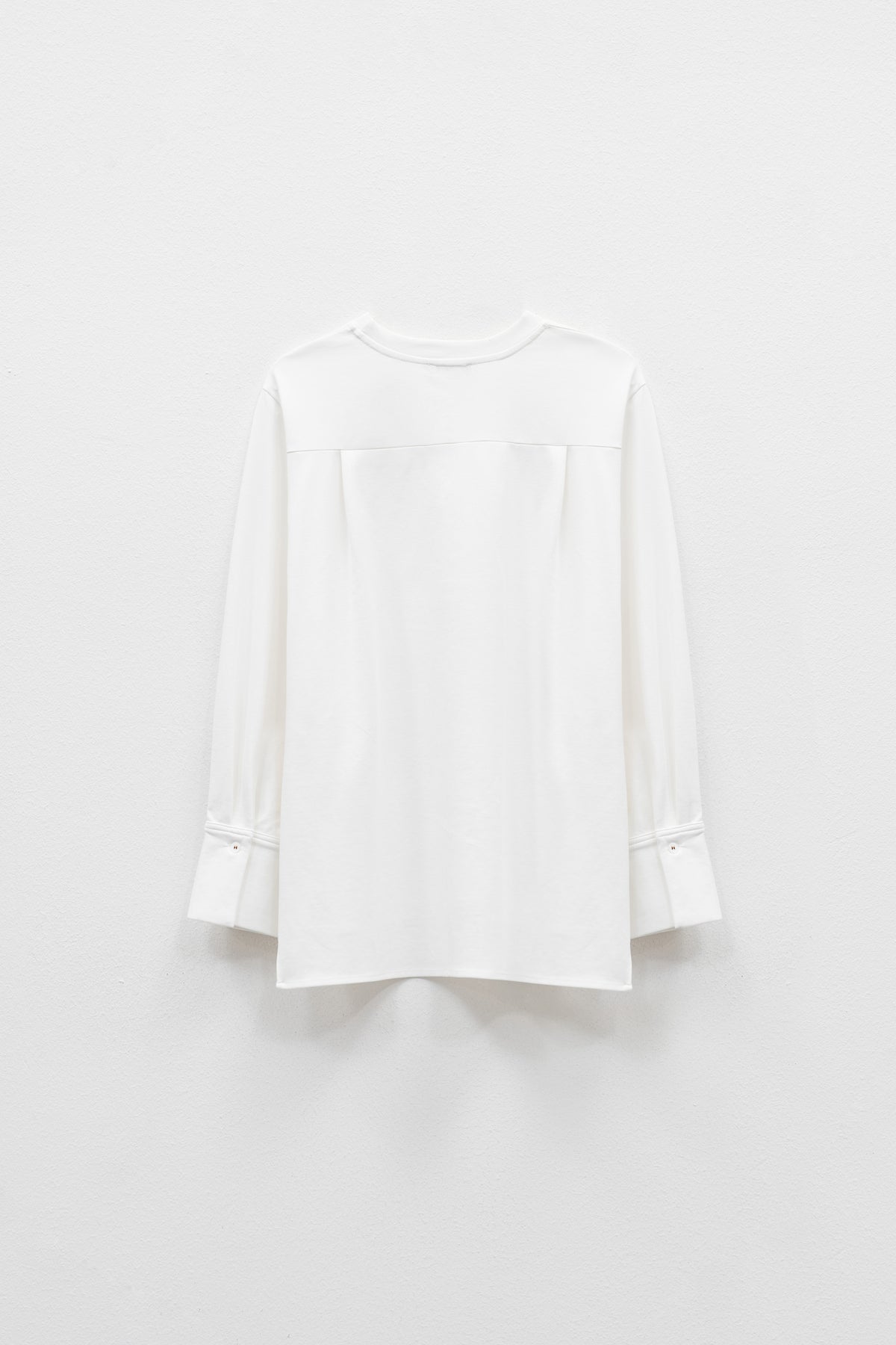 The ELEH - THE BIANCA CUFF TOP by ELEH is a plain white, long-sleeve crew neck shirt with wide sleeves, a loose fit, and an extended back hem for effortless style. Displayed against a white background, this versatile piece features a minimalist silhouette.