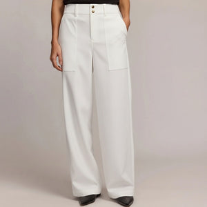 Wearing HINSON WU’s KELLY TRAVELERS TWILL PANT IN WHITE—high-waisted, wide-leg with large front pockets, front seam, and double button closure—paired with black pointed-toe shoes. Torso partially visible against a plain background.