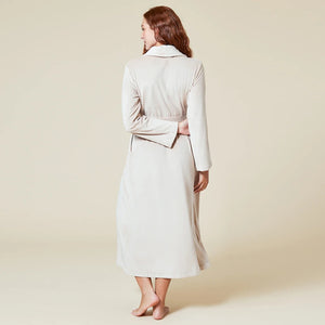 A person wearing a beige SOFTIES - SERENITY WRAP ROBE featuring a wrap silhouette with a tie waist and side pockets.