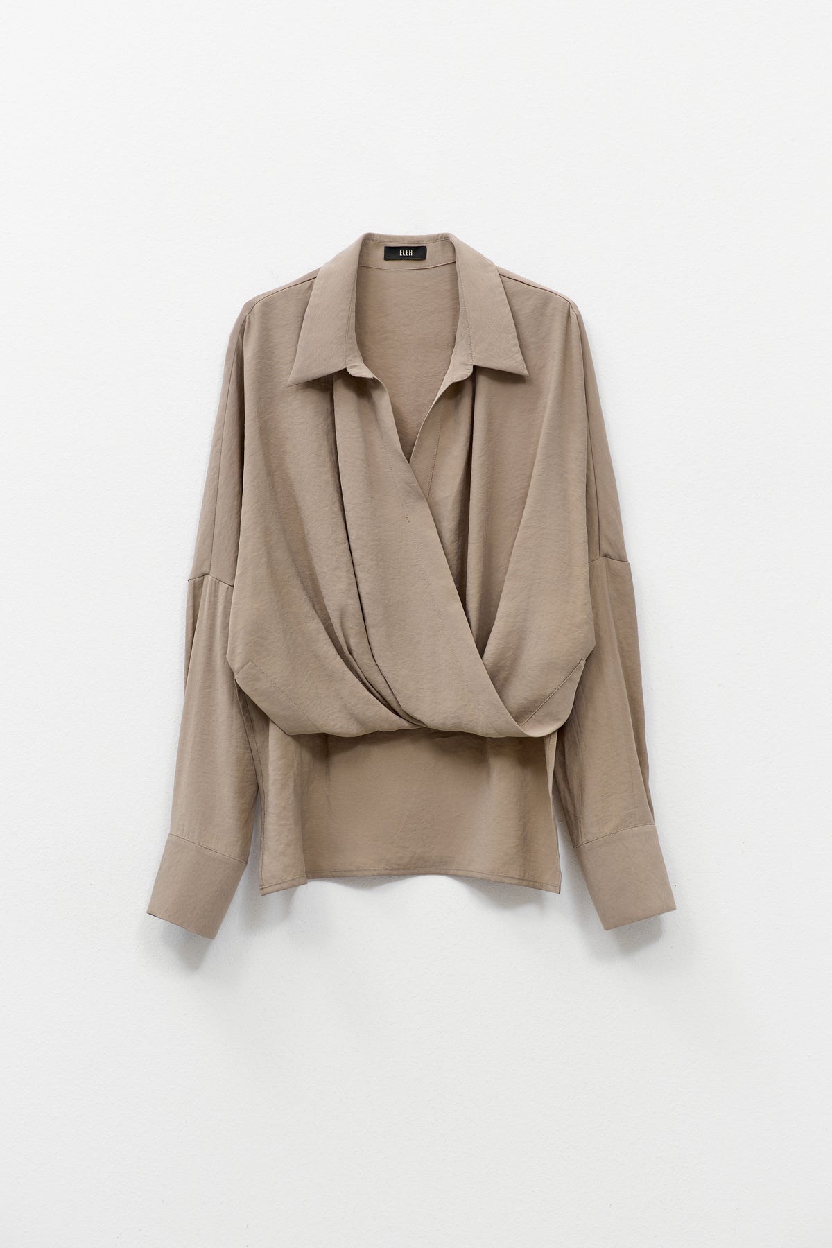 The ELEH - DRAPE FRONT BLOUSE by ELEH is a taupe Italian cotton top with a draped crossover front, wide cuffs, and a loose fit, shown against a plain white background.