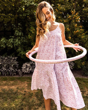 The PETITE PLUME - DORSET FLORAL CHLOE NIGHTGOWN is a sleeveless, white sundress with thin straps, reminiscent of luxurious sleepwear. It showcases a flowing, tiered design adorned with a delicate pink floral pattern. Made from the finest quality cotton, the fabric is lightweight and airy, perfect for warm weather. Displayed against a white background.