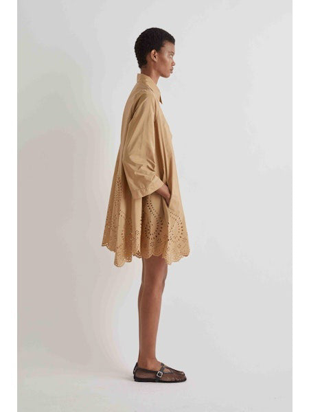 A person stands against a white background wearing the MEIMEIJ Lasercut Cotton Shirt Dress featuring eyelet embroidery and scalloped cuff hems, paired with black flat shoes.