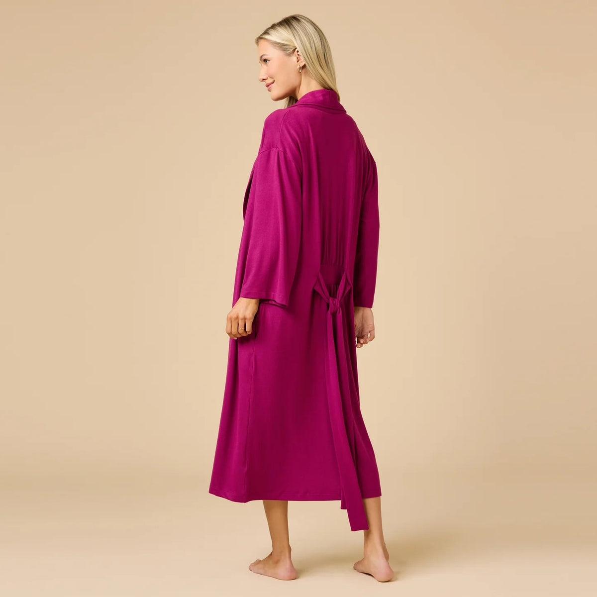 A woman wears a SOFTIES - DREAM SHAWL COLLAR ROBE in pink and white stripes, featuring a shawl collar, a tie waist, and three-quarter length sleeves.