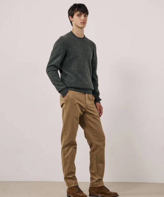 A young man with short dark hair wears the HARTFORD Seamless Wool Crew Pullover in Camo Green and tan pants, standing against a plain light-colored background, looking slightly to the side with a neutral expression.