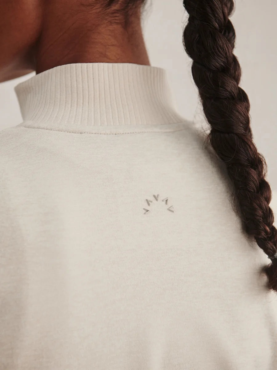A person wears a light beige Varley Rufus Cropped Zip Through Sweat in Pebble Marl with a high collar and matching pants.