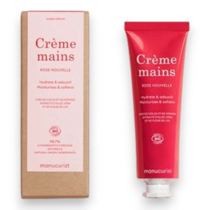 With perfectly manicured nails, a person applies MANUCURIST - COSMOS ORGANIC HAND CREAM, ROSE NOUVELLE from MANUCURIST INC to the back of their hand against a soft pink background, emphasizing the importance of caring for hands and nails.