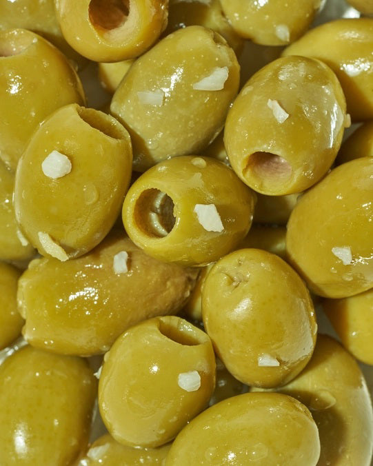 A yellow packet of FREESTYLE - LEMON GARLIC GREEN OLIVES from FREESTYLE SNACKS, featuring green olives flavored with extra virgin olive oil. The packaging highlights the "all-natural" ingredients and notes that the olives are "grown in Greece." Weighing 4 oz (113g), the pack showcases images of green olives alongside phrases such as "pitted &amp; unpasteurized" and "healthy snacking on the go.