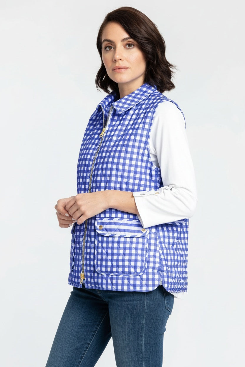 A woman with short dark hair stands sideways and looks at the camera against a plain white background, wearing the HINSON WU LAUREN REVERSIBLE VEST— a blue and white checkered quilted cotton vest by HINSON WU— layered over a white long-sleeve shirt and jeans.