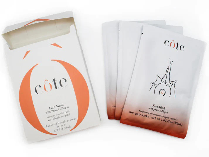 A white rectangular box partially open at the top, revealing multiple sheet masks inside, along with a special foot mask for age-defying hydration. The box is labeled with the brand name "COTE" and adorned with orange design accents. It contains "COTE - FOOT MASK WITH COLLAGEN 3 PACK.