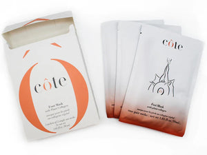 A white rectangular box partially open at the top, revealing multiple sheet masks inside, along with a special foot mask for age-defying hydration. The box is labeled with the brand name "COTE" and adorned with orange design accents. It contains "COTE - FOOT MASK WITH COLLAGEN 3 PACK.