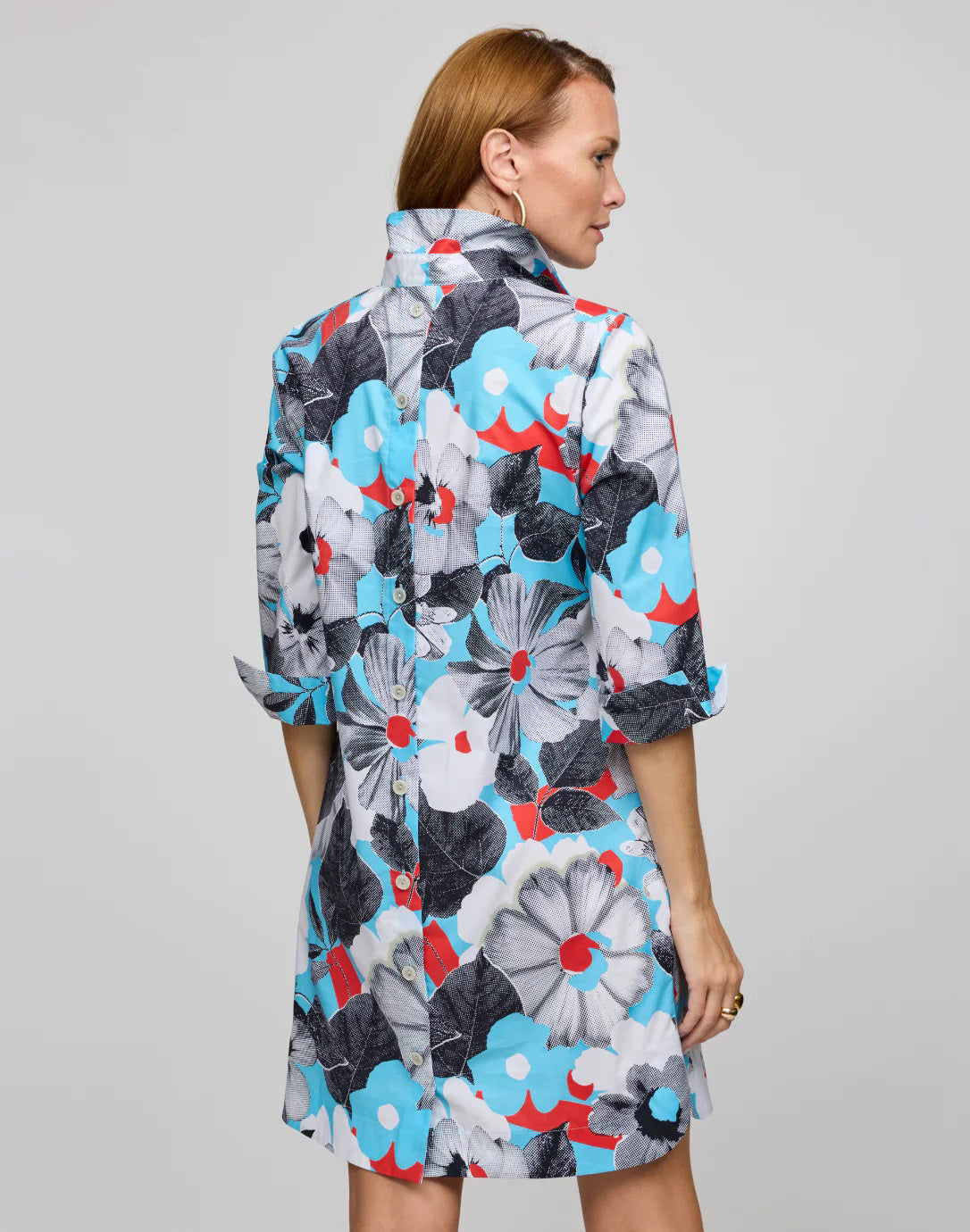 The person is wearing the HINSON WU Aileen dress, featuring a knee-length cut in stretch polished cotton with a pop art flower print in blue, black, white, and red. It has a collared neckline and three-quarter sleeves, stylishly set against a plain gray background.