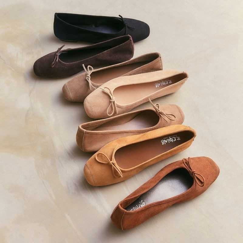 The REQINS HARMONY suede ballerina flats in Marron feature a dark brown finish and a small bow on the toe, shown in side profile against a plain light background—a timeless choice for any classic wardrobe.