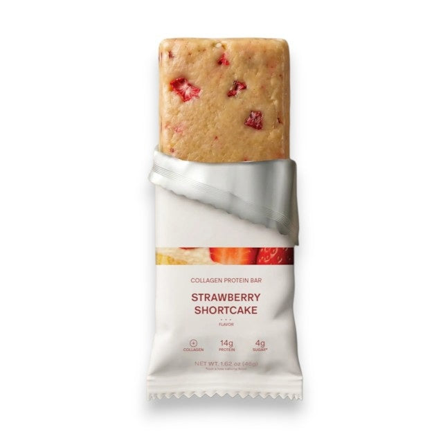 A STARS+HONEY - STRAWBERRY SHORTCAKE Collagen Protein Bar wrapper bursts open, releasing strawberries, cake pieces, and swirls of whipped cream against a neutral background—perfectly capturing the delicious essence of this wholesome treat. Enjoy all the flavor you love in strawberry shortcake, now in a nourishing STARS+HONEY Collagen Protein Bar.