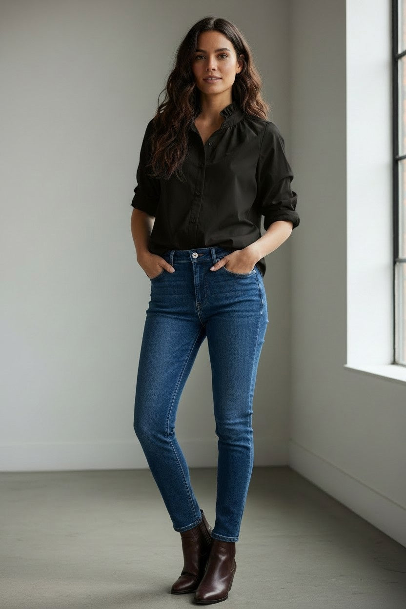 A woman styles the KMJ - SOUTHERN LOVER SHIRT, a black blouse with puff sleeves and ruffle collar by KMJ, with blue jeans, layered gold jewelry, and red lipstick. Her wavy dark hair completes this Southern-inspired look.