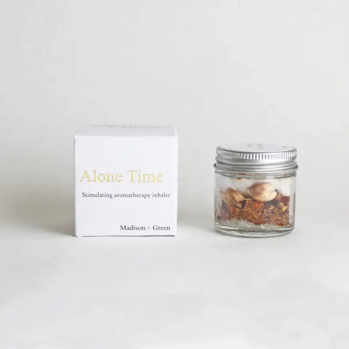 The MADISON GREEN ALONE TIME AROMATHERAPY INHALER is a small glass jar with a white lid, featuring a stress-relief blend of herbs and organic essential oils—perfect for aromatherapy.
