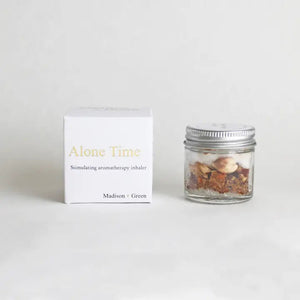 The MADISON GREEN ALONE TIME AROMATHERAPY INHALER is a small glass jar with a white lid, featuring a stress-relief blend of herbs and organic essential oils—perfect for aromatherapy.